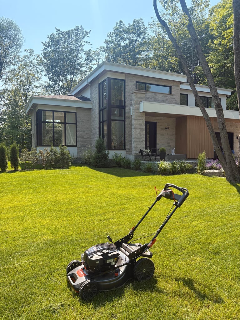 Lawn mower on manicured grass in front of modern two-story residential home with stone and metal exterior