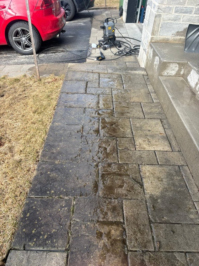 Entrée de cour mouillée avec équipement de lavage haute pression installé sur une surface pavée, voiture rouge garée en arrière-plan